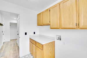 Laundry area with light hardwood / wood-style flooring, hookup for a washing machine, and cabinets