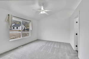 Carpeted empty room featuring lofted ceiling and ceiling fan