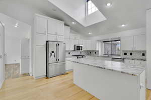 Kitchen with a center island, white cabinetry, stainless steel appliances, and light wood-type flooring