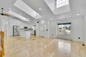 Unfurnished living room with lofted ceiling with skylight, light wood-type flooring, and ceiling fan