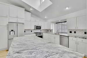 Kitchen featuring white cabinetry, light stone countertops, vaulted ceiling, sink, and high end appliances