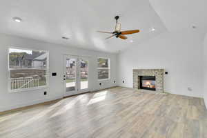 Unfurnished living room featuring a stone fireplace, vaulted ceiling, a textured ceiling, light hardwood / wood-style floors, and ceiling fan