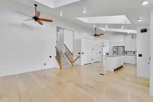 Unfurnished living room featuring vaulted ceiling with skylight and light wood-type flooring