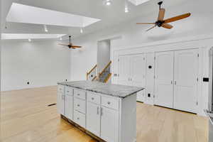 Kitchen featuring light hardwood / wood-style flooring, light stone countertops, a center island, white cabinets, and ceiling fan