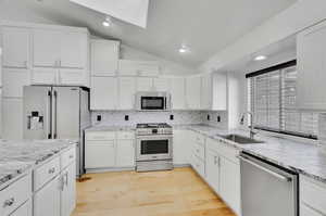 Kitchen featuring tasteful backsplash, appliances with stainless steel finishes, white cabinetry, vaulted ceiling, and light hardwood / wood-style floors