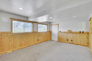 Empty room featuring a textured ceiling, light colored carpet, and wooden walls