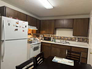 Kitchen with a textured ceiling, dark brown cabinets, sink, and white appliances