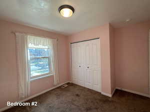 Unfurnished bedroom featuring dark colored carpet, a textured ceiling, and a closet