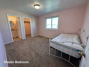 Unfurnished bedroom featuring ensuite bathroom, a textured ceiling, light carpet, and a walk in closet