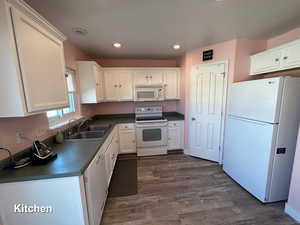 Kitchen featuring white cabinets, white appliances, dark hardwood / wood-style floors, and sink