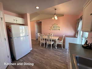 Kitchen with white fridge, sink, vaulted ceiling, white cabinets, and dark wood-type flooring