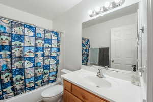 Full bathroom with toilet, vanity, and shower / bathtub combination with curtain