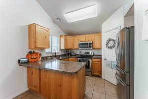 Kitchen with kitchen peninsula, stainless steel appliances, sink, vaulted ceiling, and light tile patterned floors