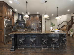 Kitchen with a kitchen breakfast bar, hanging light fixtures, a large island, and custom range hood