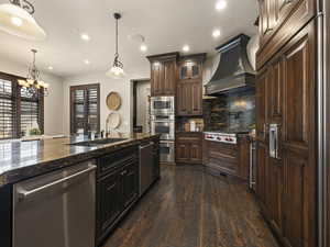 Kitchen featuring appliances with stainless steel finishes, decorative light fixtures, premium range hood, and dark hardwood / wood-style flooring