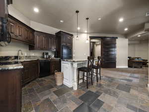 Kitchen featuring a kitchen island, a kitchen breakfast bar, a barn door, black appliances, and decorative light fixtures