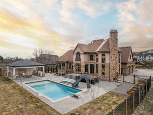 Pool at dusk featuring a jacuzzi, a diving board, exterior kitchen, a water slide, and a patio