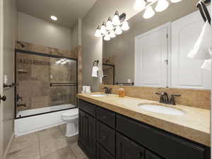 Full bathroom featuring vanity, bath / shower combo with glass door, toilet, and tile patterned flooring