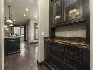 Bar featuring decorative light fixtures, dark wood-type flooring, and dark stone counters