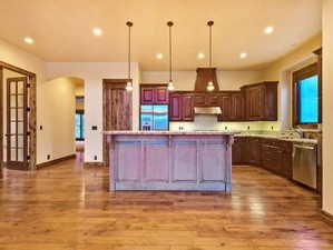 Kitchen featuring appliances with stainless steel finishes, hardwood / wood-style floors, decorative light fixtures, and a kitchen island