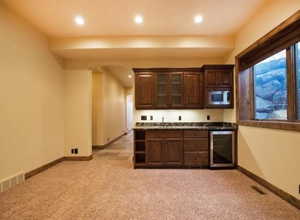 Bar featuring stainless steel microwave, sink, dark brown cabinetry, light colored carpet, and beverage cooler