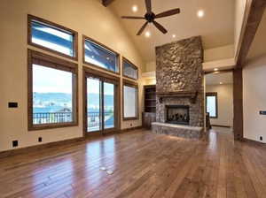 Unfurnished living room featuring hardwood / wood-style flooring, high vaulted ceiling, a mountain view, and a stone fireplace