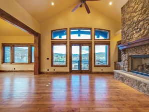 Unfurnished living room with ceiling fan, high vaulted ceiling, hardwood / wood-style flooring, and a stone fireplace