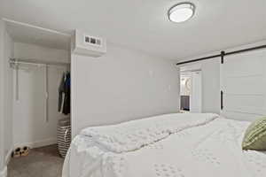 Bedroom with a closet, a textured ceiling, a barn door, and new carpet