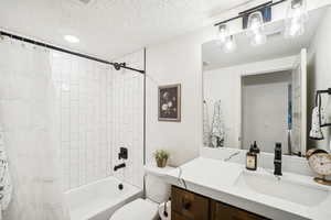 Full bathroom featuring vanity, a textured ceiling, shower / bath combo with shower curtain, and toilet