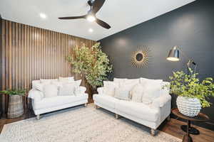 Living room with ceiling fan, wood-type flooring, and wooden walls