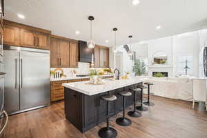 Kitchen featuring a kitchen island with sink, dark hardwood / wood-style floors, hanging light fixtures, stainless steel appliances, and custom exhaust hood