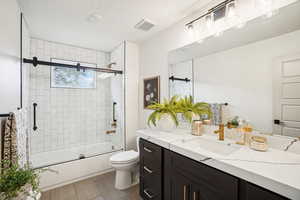 Full bathroom featuring toilet, enclosed tub / shower combo, vanity, and a textured ceiling