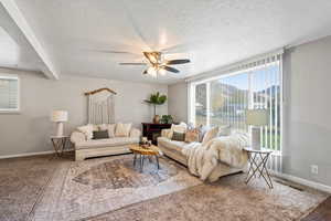 Carpeted living room with a textured ceiling, beam ceiling, and ceiling fan