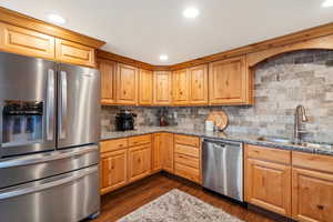 Kitchen with decorative backsplash, light stone countertops, dark wood-type flooring, sink, and stainless steel appliances