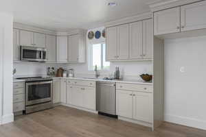 Kitchen with sink, appliances with stainless steel finishes, light hardwood / wood-style flooring, and white cabinetry