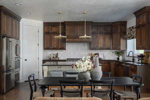 Kitchen with hanging light fixtures, dark hardwood / wood-style flooring, stainless steel appliances, dark brown cabinetry, and sink