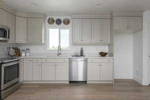 Kitchen with light hardwood / wood-style flooring, white cabinets, stainless steel appliances, and sink