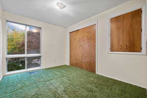 Unfurnished bedroom with a textured ceiling, multiple windows, and carpet floors