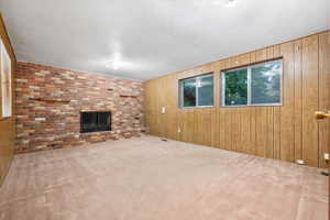 Unfurnished living room featuring light colored carpet, wooden walls, and a fireplace