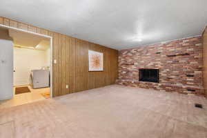 Unfurnished living room with washer / dryer, wood walls, and light colored carpet