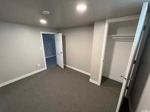 Unfurnished bedroom with a closet, a textured ceiling, modern lighting, and dark carpet