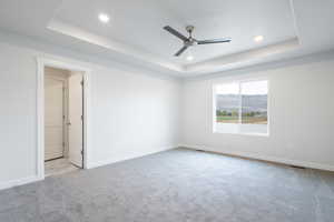 Spare room featuring ceiling fan, a tray ceiling, and light colored carpet