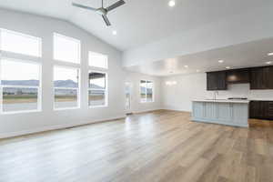 Unfurnished living room featuring lofted ceiling, a mountain view, ceiling fan with notable chandelier, and light wood-type flooring