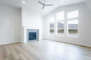 Unfurnished living room with high vaulted ceiling, a tile fireplace, light wood-type flooring, and ceiling fan