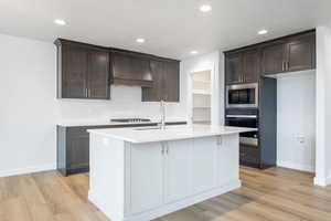 Kitchen with an island with sink, stainless steel appliances, light hardwood / wood-style floors, and tasteful backsplash