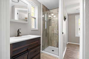 Bathroom with a shower with door, vanity, wood-type flooring, and a healthy amount of sunlight