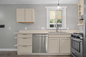 Kitchen featuring sink, cream cabinetry, hanging light fixtures, stainless steel appliances, and dark wood-type flooring