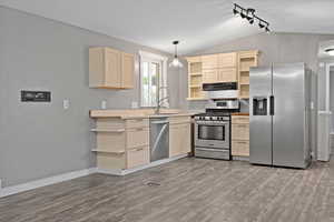 Kitchen featuring sink, stainless steel appliances, vaulted ceiling, decorative light fixtures, and light hardwood / wood-style flooring