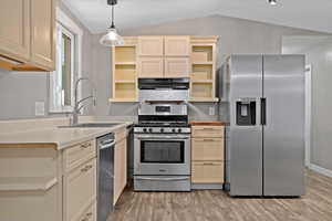 Kitchen featuring stainless steel appliances, sink, vaulted ceiling, decorative light fixtures, and light hardwood / wood-style floors