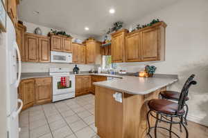 Kitchen with a kitchen bar, kitchen peninsula, white appliances, and light tile patterned floors